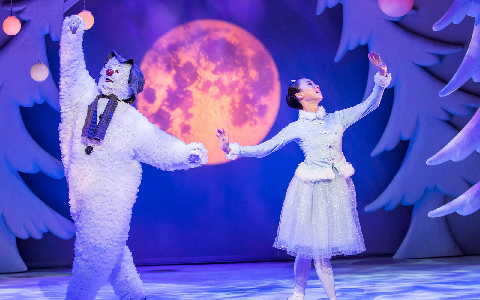 Snowman and dancer performing on stage with a moon backdrop.