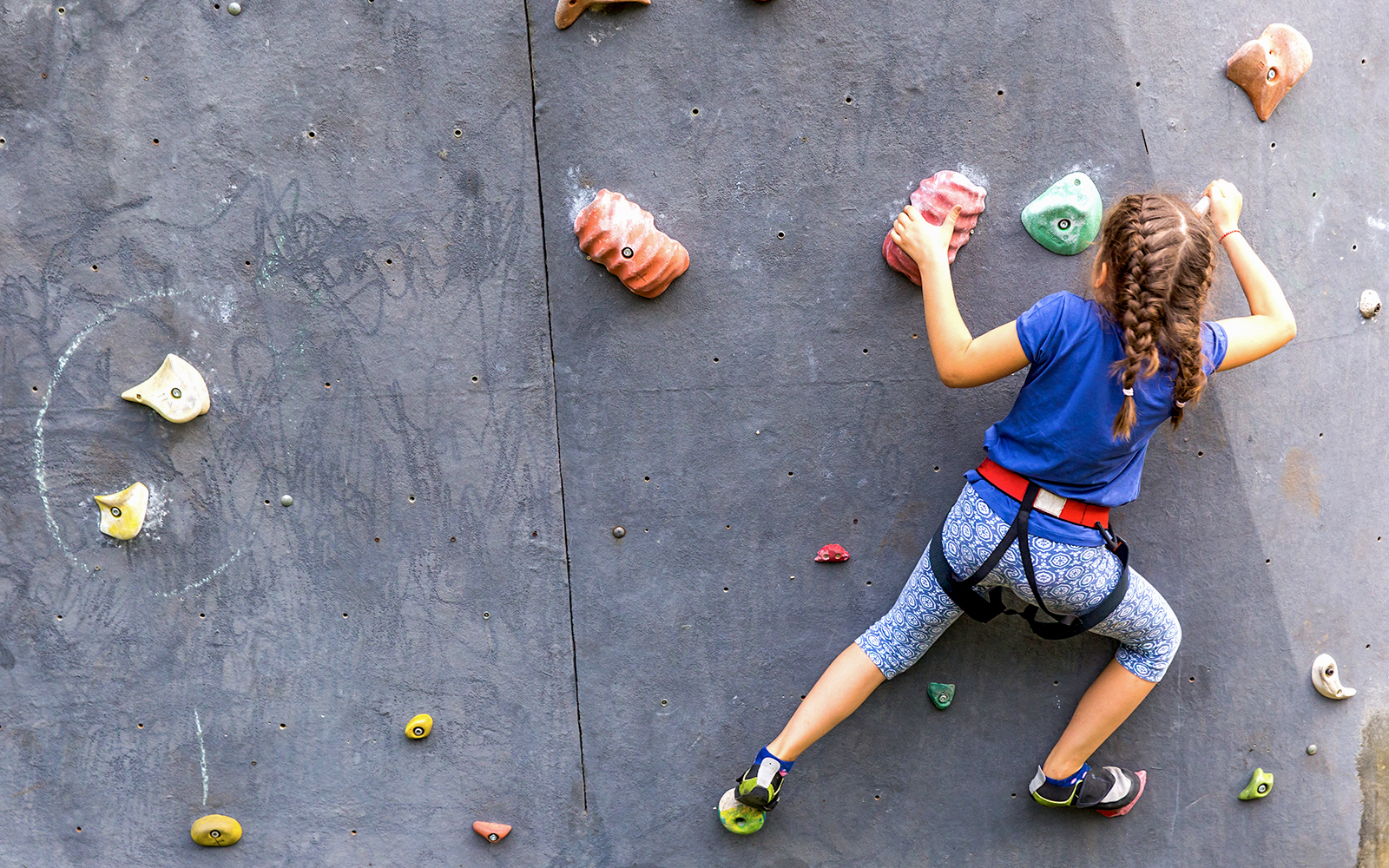 Young girl climbing an artificial rock wall with colorful holds.