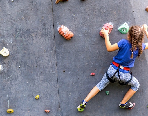 Young girl climbing an artificial rock wall with colorful holds.