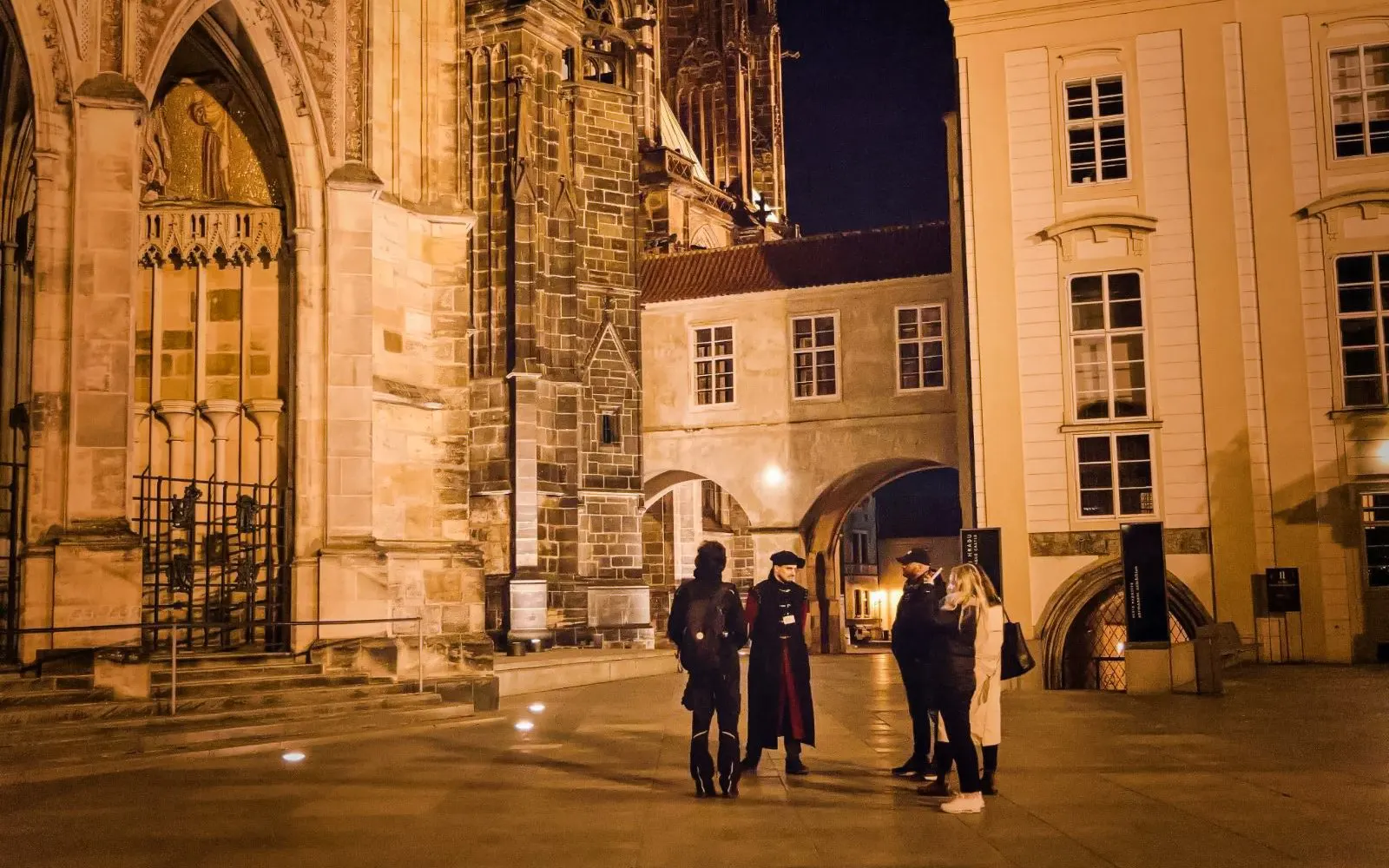 Group on a guided tour at night near Prague Castle's historic architecture.