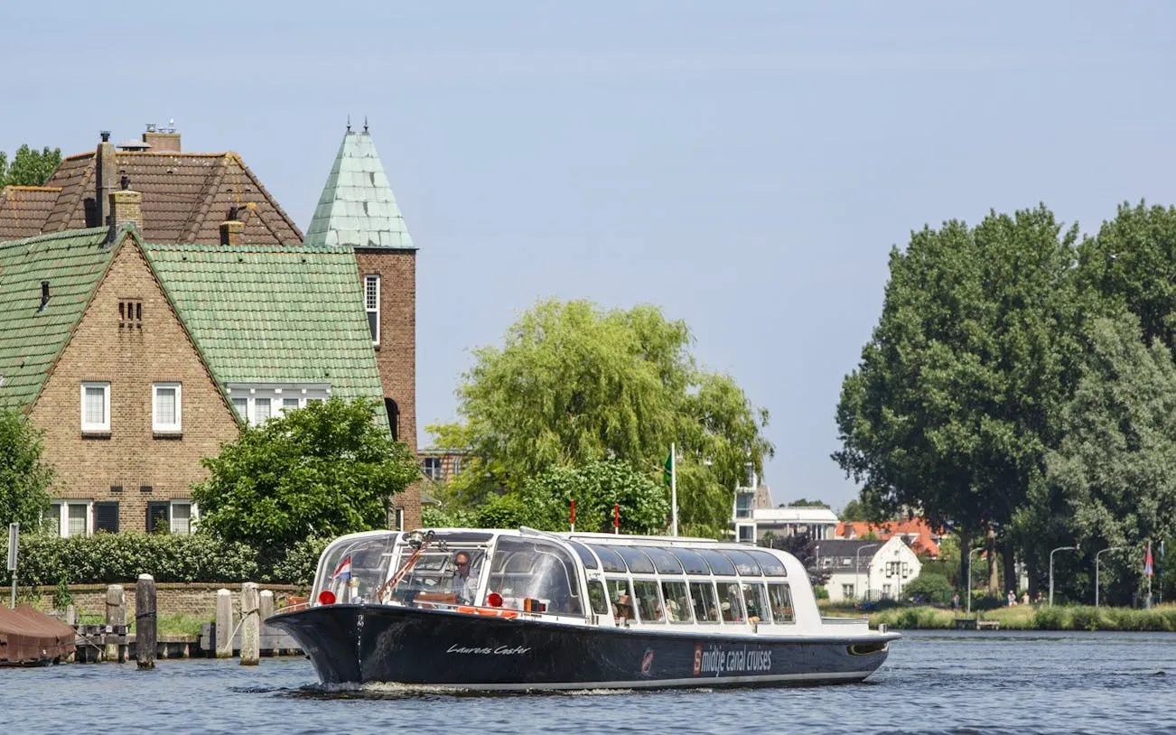 Haarlem canal cruise boat passing historical buildings and lush greenery.