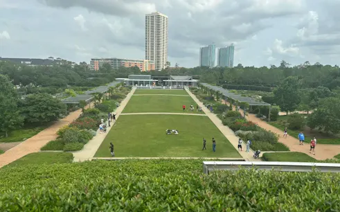 Houston Museum District park with visitors walking along pathways, tall buildings in the background.