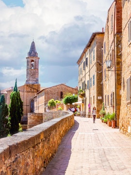 Stone path leading to Pienza with historic buildings and bell tower in Tuscany, Italy.