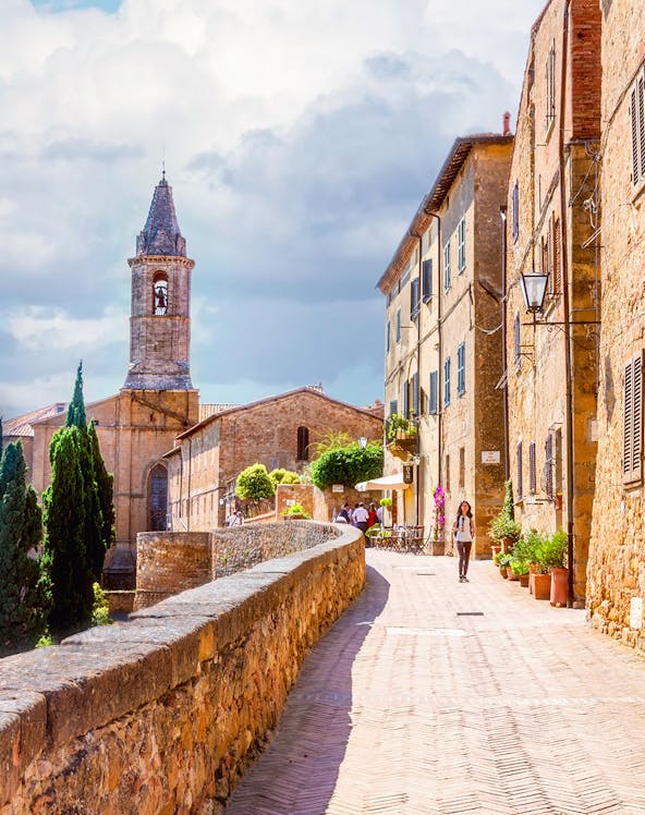 Stone path leading to Pienza with historic buildings and bell tower in Tuscany, Italy.
