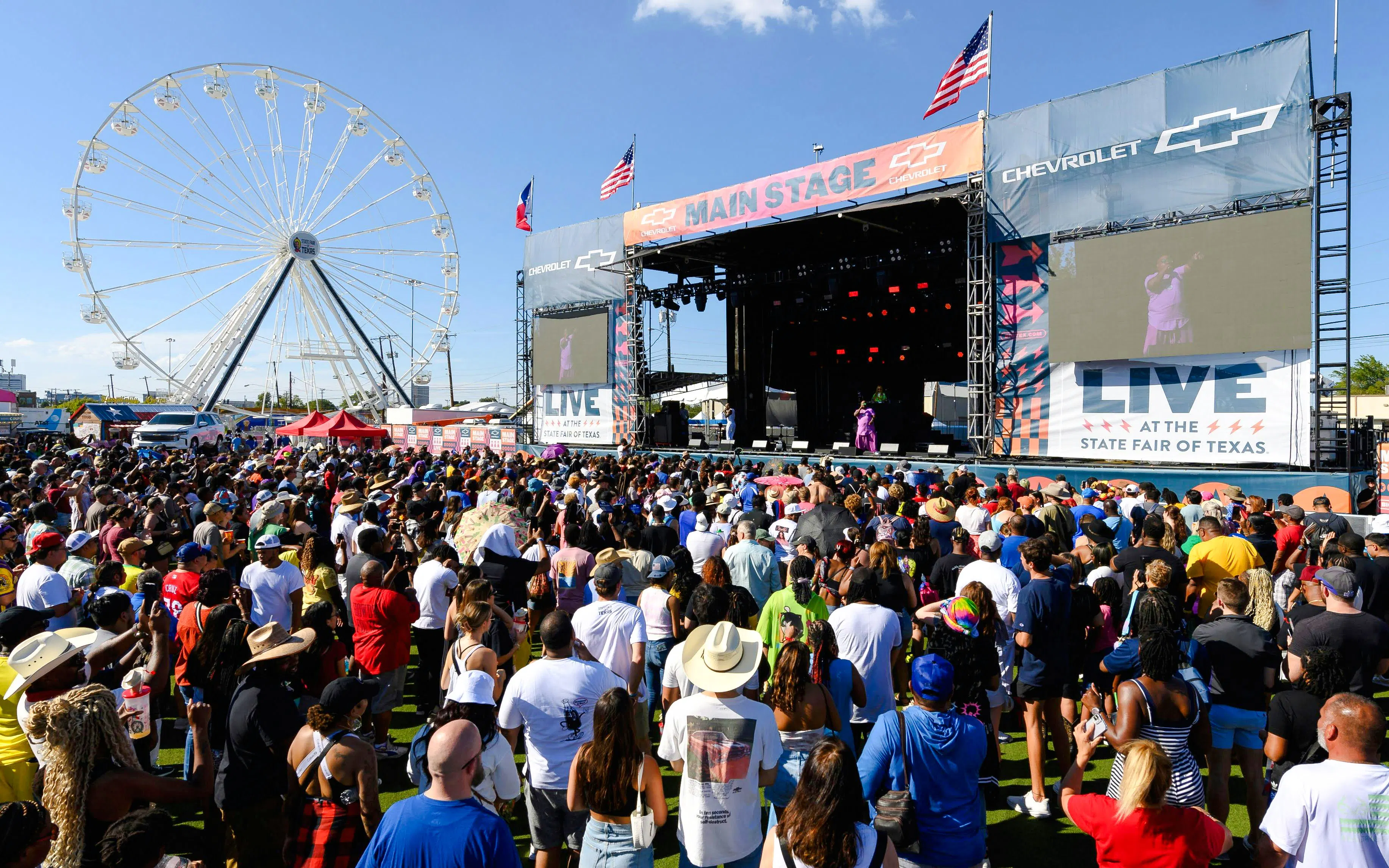 Crowd enjoying a live performance at the State Fair of Texas with Ferris wheel in background.