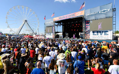 Crowd enjoying a live performance at the State Fair of Texas with Ferris wheel in background.