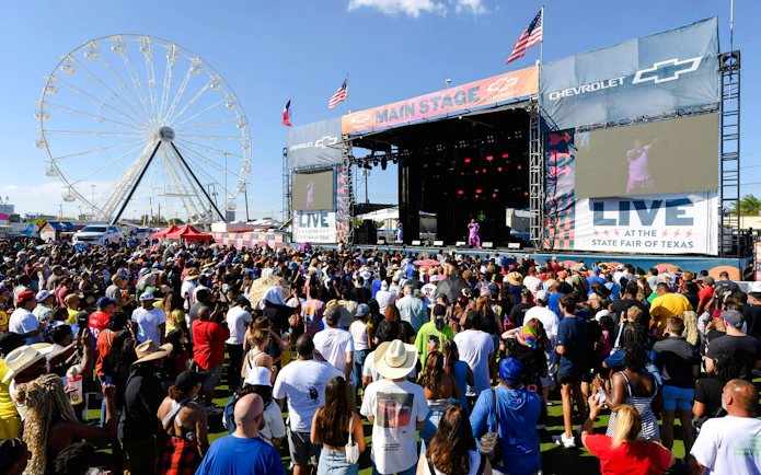 Crowd enjoying a live performance at the State Fair of Texas with Ferris wheel in background.