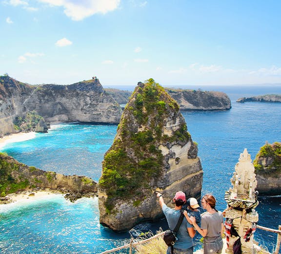 Young family admiring Thousand Islands Viewpoint, Nusa Penida, Bali, with ocean and cliffs in background.