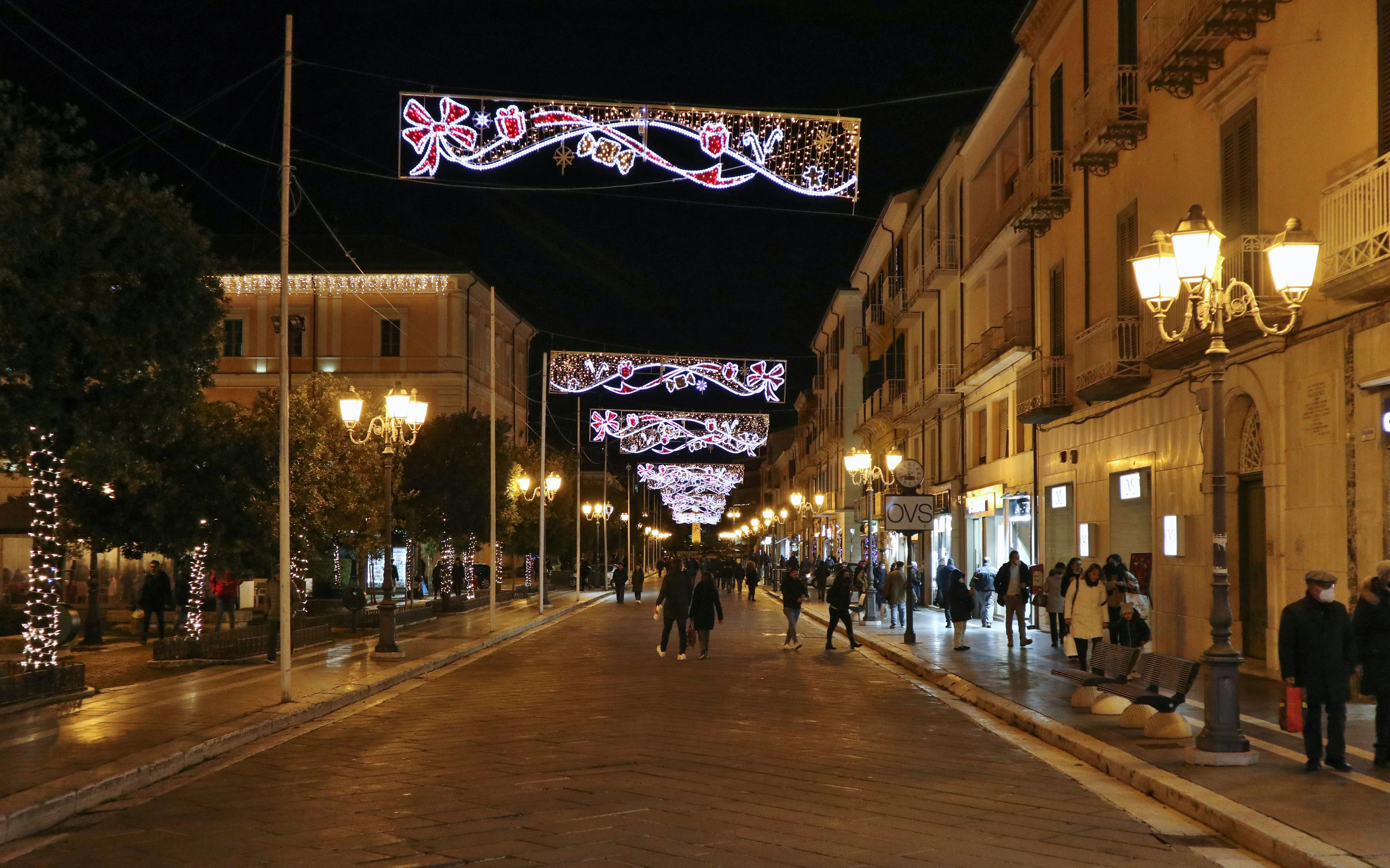 Pedestrians walking under festive lights on a street near Galleria Vittorio Emanuele II, Milan at night.