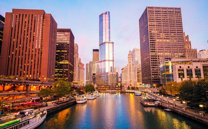 Moored tour boats on the Chicago River at sunrise with city skyline.