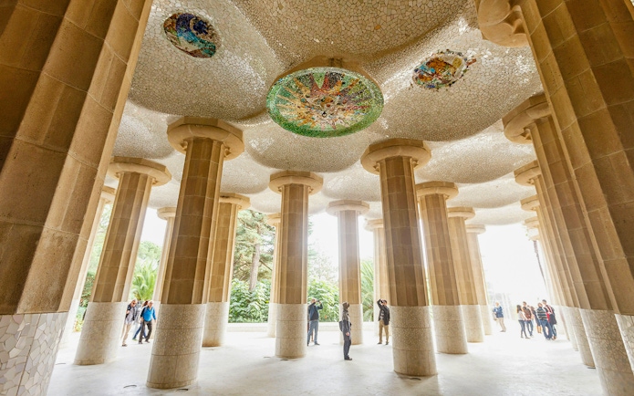 Tourists exploring the mosaic ceiling and columns at Park Guell, Barcelona.