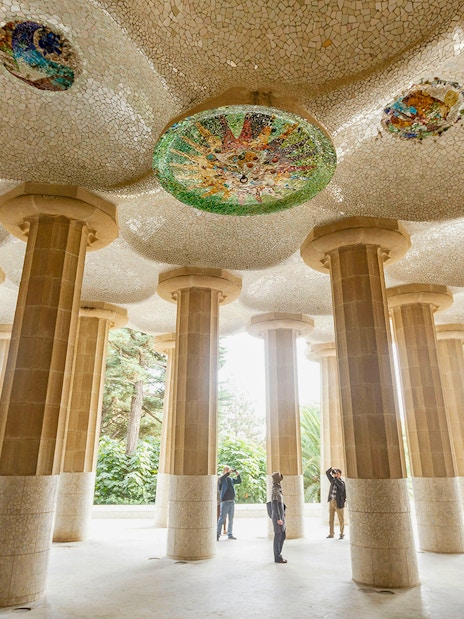 Tourists exploring the mosaic ceiling and columns at Park Guell, Barcelona.
