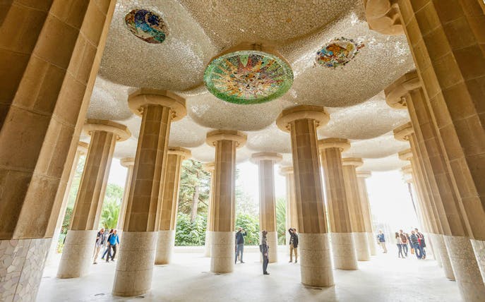 Tourists exploring the mosaic ceiling and columns at Park Guell, Barcelona.