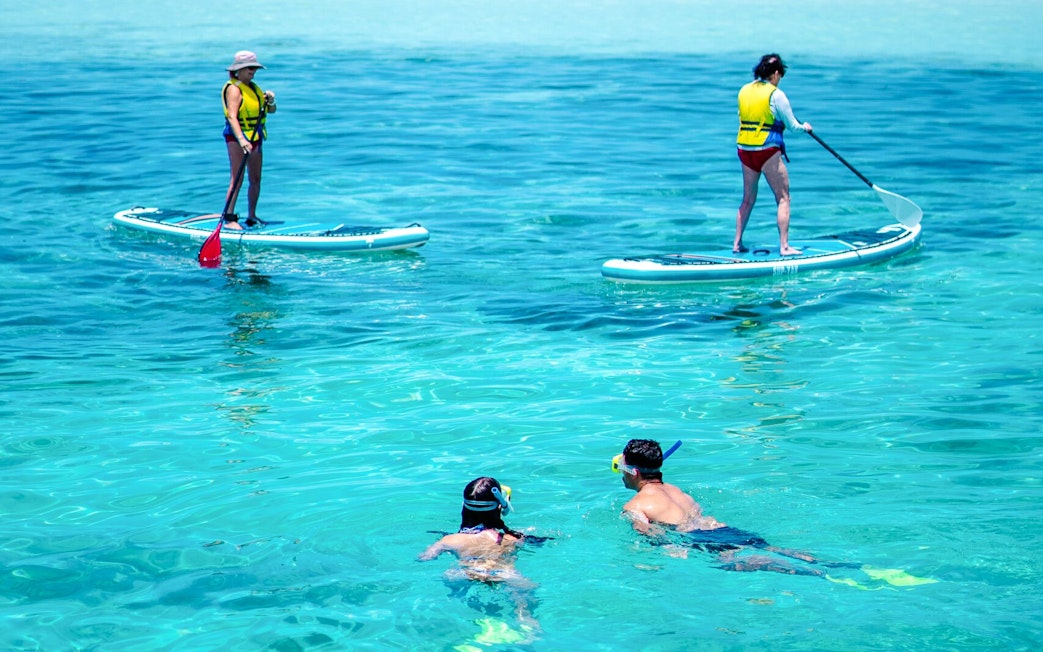 Paddle surfers and snorkelers enjoying clear waters at South Sea Cats, Fiji.