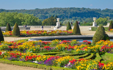 Tourists walking in Versailles Palace garden with vibrant flower beds.