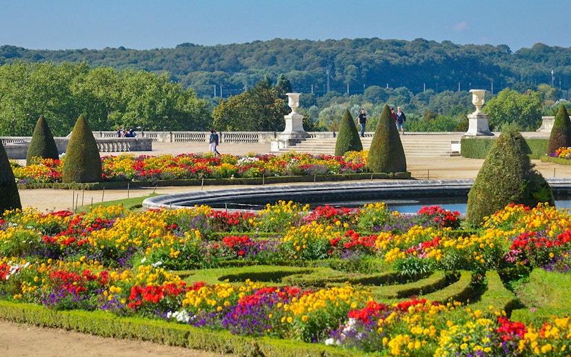 Tourists walking in Versailles Palace garden with vibrant flower beds.
