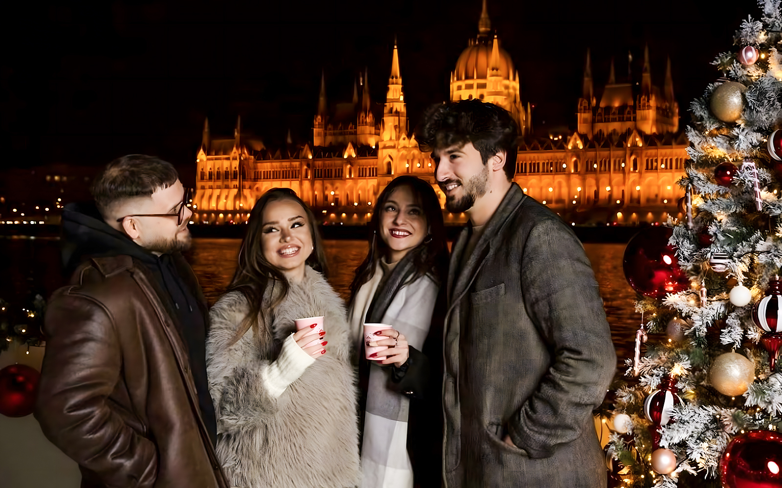 People enjoying a Christmas Market Cruise in Budapest with the Parliament building illuminated at night.