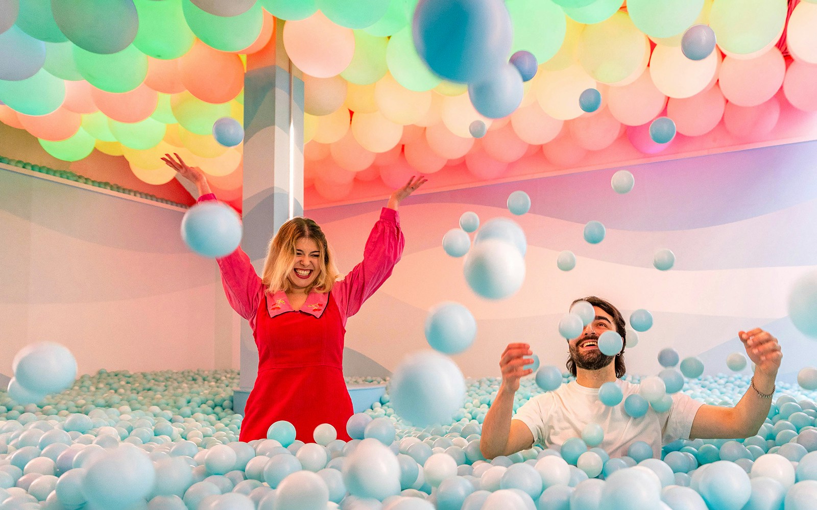 People enjoying a colorful ball pit experience indoors.