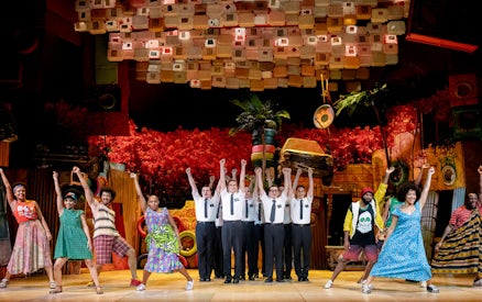 Performers on stage during The Book of Mormon musical, vibrant set design in background.