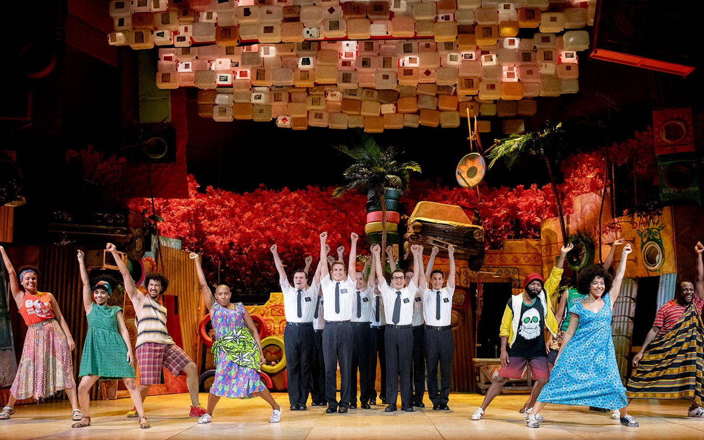 Performers on stage during The Book of Mormon musical, vibrant set design in background.