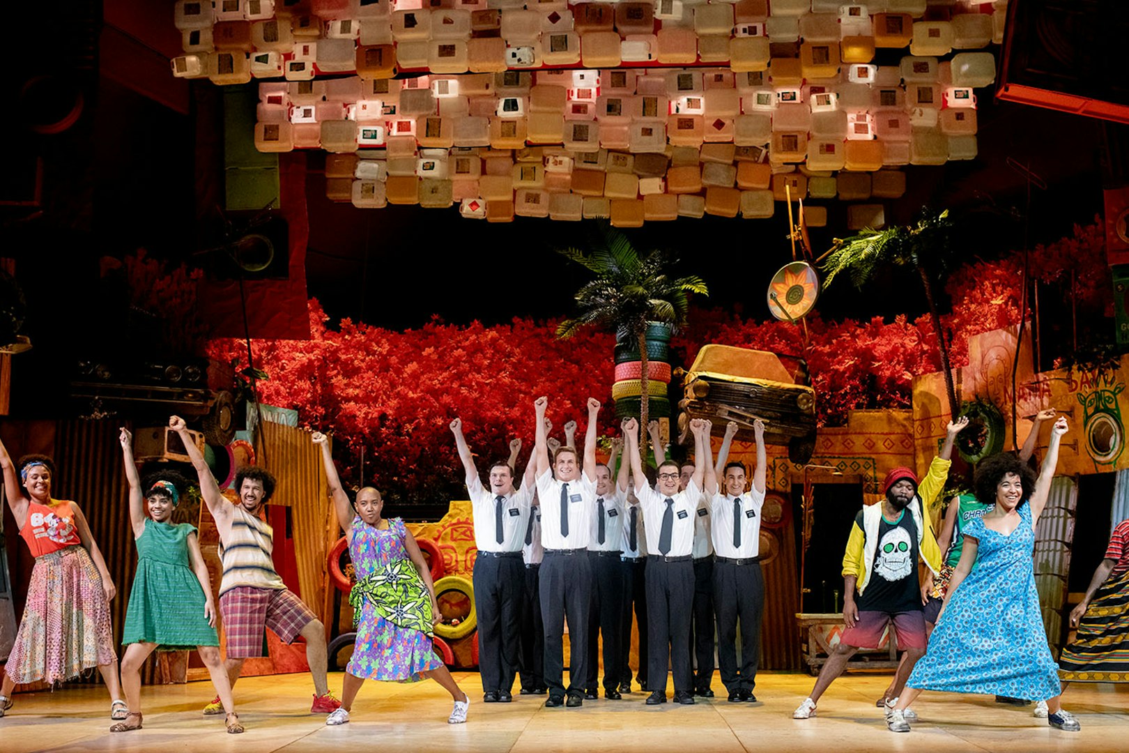 Performers on stage during The Book of Mormon musical, vibrant set design in background.