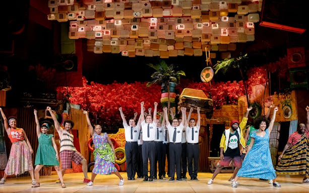 Performers on stage during The Book of Mormon musical, vibrant set design in background.
