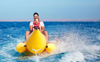 Father and daughter enjoying a banana boat ride on the ocean during summer vacation.