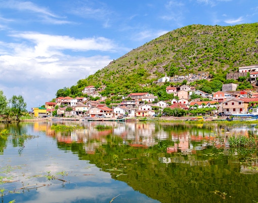 Vranjina fishing village by Skadar Lake, Montenegro, with hillside houses and lake reflection.