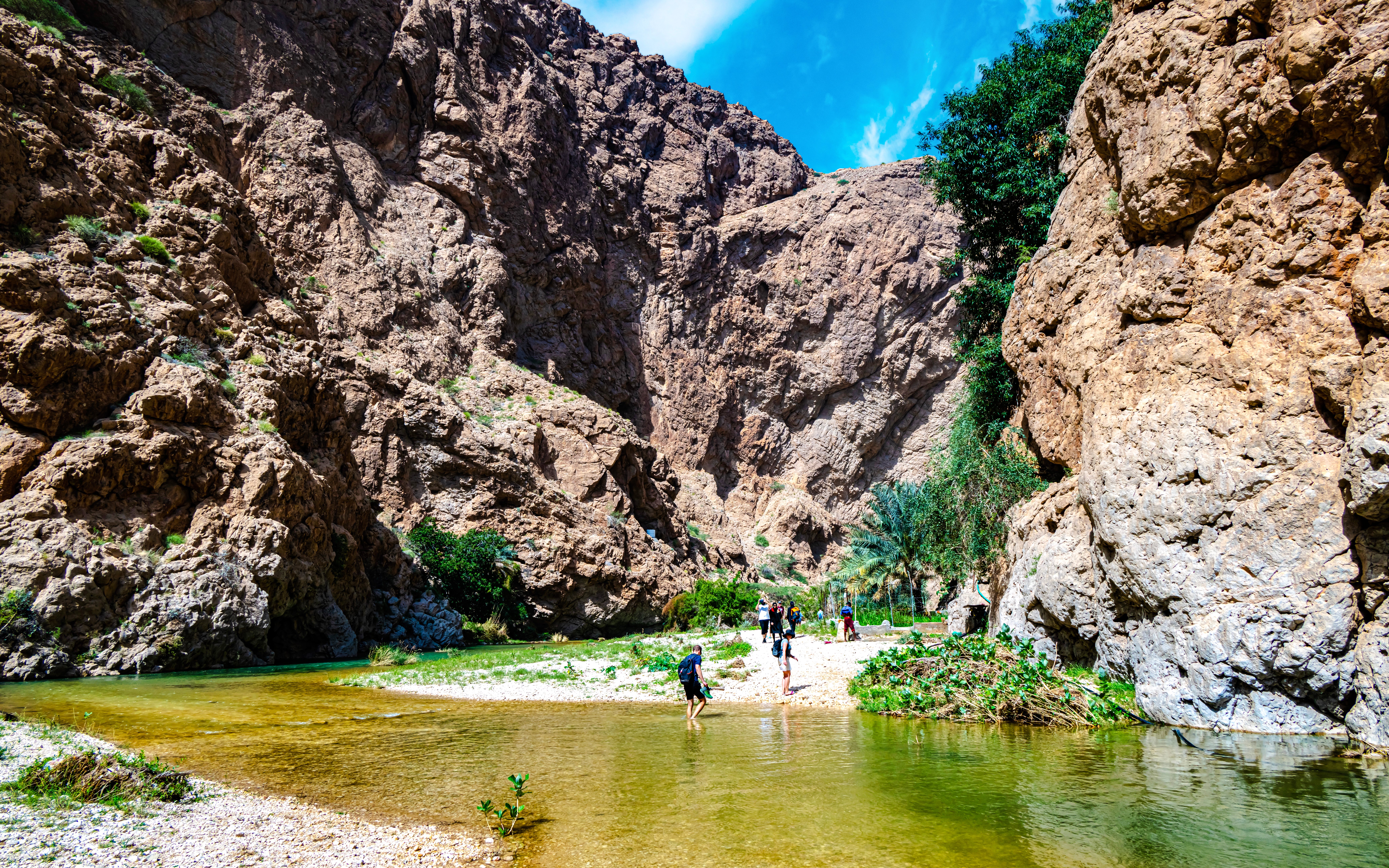 Wadi Ash Shab canyon with hikers crossing a shallow stream in Southeastern Governorate, Oman.