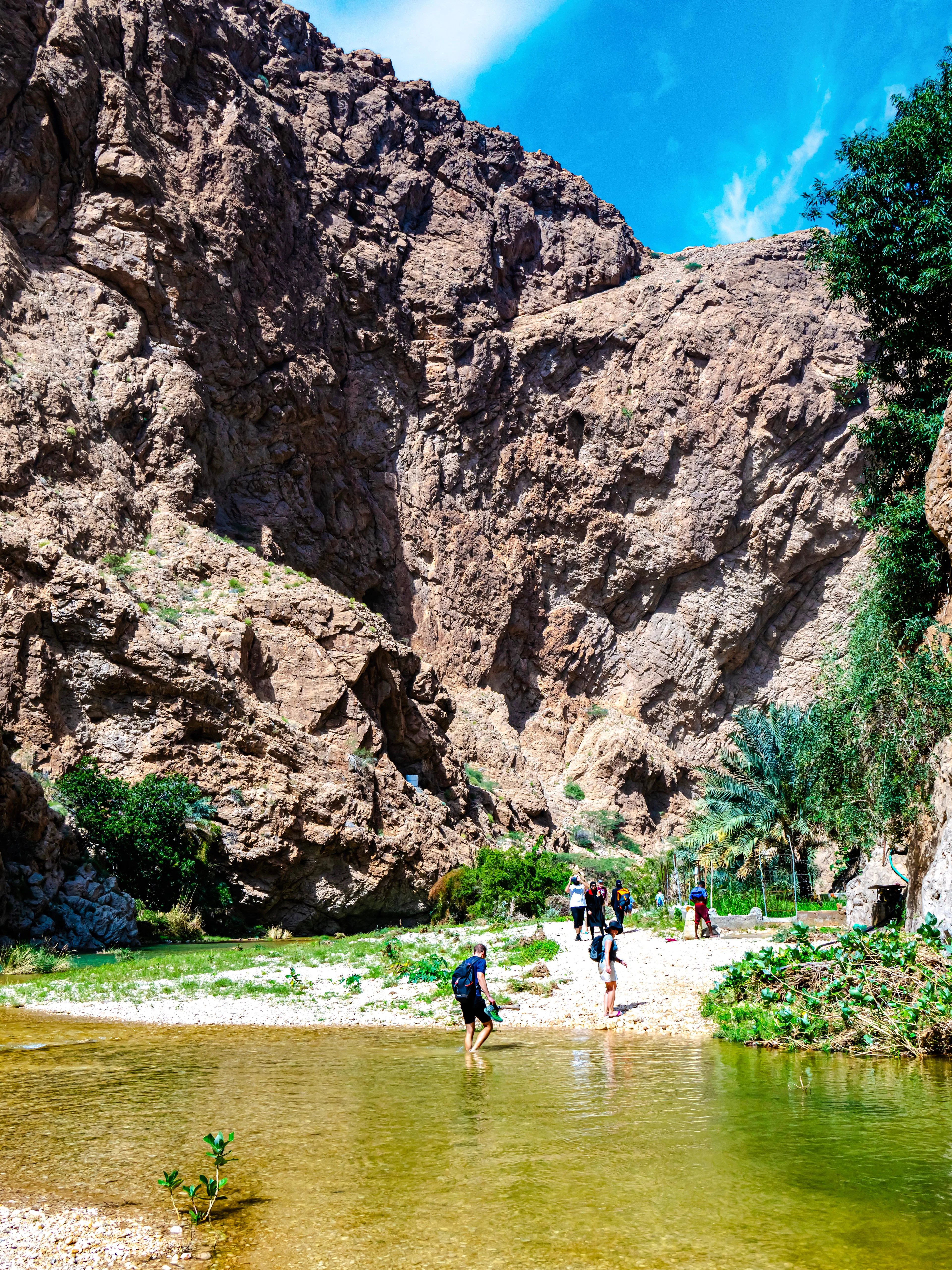 Wadi Ash Shab canyon with hikers crossing a shallow stream in Southeastern Governorate, Oman.