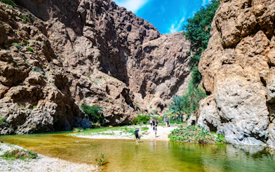 Wadi Ash Shab canyon with hikers crossing a shallow stream in Southeastern Governorate, Oman.