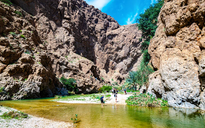 Wadi Ash Shab canyon with hikers crossing a shallow stream in Southeastern Governorate, Oman.