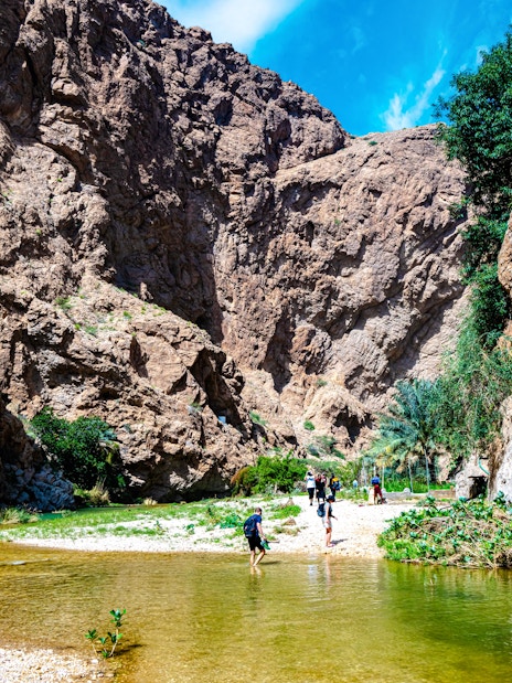 Wadi Ash Shab canyon with hikers crossing a shallow stream in Southeastern Governorate, Oman.