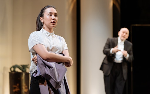 Theater scene from "Bitter Wheat" with a woman holding a coat and a man in the background.