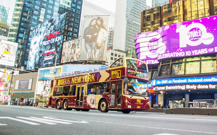 Big Bus tour passing through Times Square, New York City, with bright billboards.