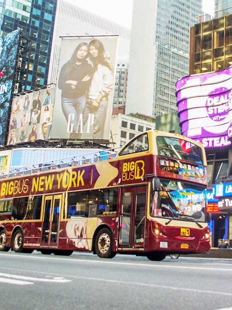 Big Bus tour passing through Times Square, New York City, with bright billboards.