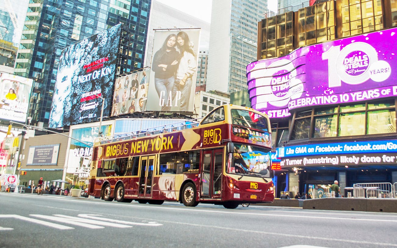 Big Bus tour passing through Times Square, New York City, with bright billboards.