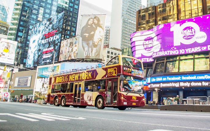 Big Bus tour passing through Times Square, New York City, with bright billboards.