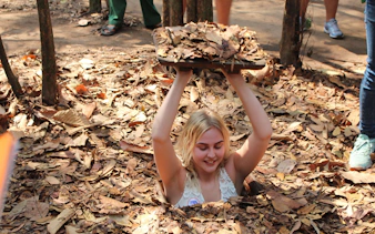 Visitor emerging from a hidden entrance at Cu Chi Tunnels during VIP speed boat tour.