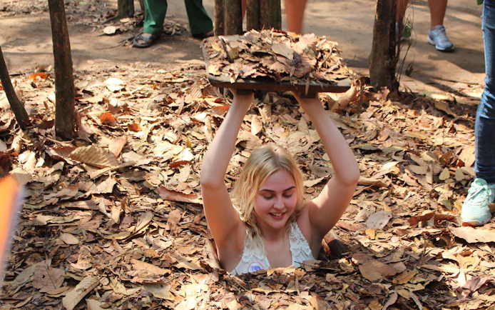 Visitor emerging from a hidden entrance at Cu Chi Tunnels during VIP speed boat tour.