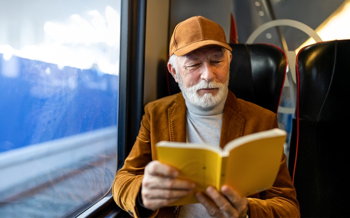 Senior man reading a book on a train journey.