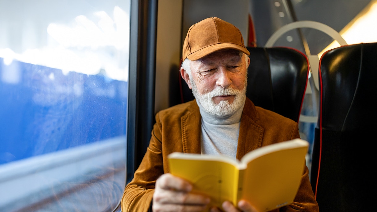 Senior man reading a book on a train journey.