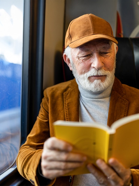 Senior man reading a book on a train journey.