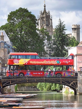 Cambridge sightseeing bus crossing a bridge with historic church in the background.