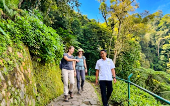 Tourists walking with a guide on a forest path near Curug Cimahi, Bandung.