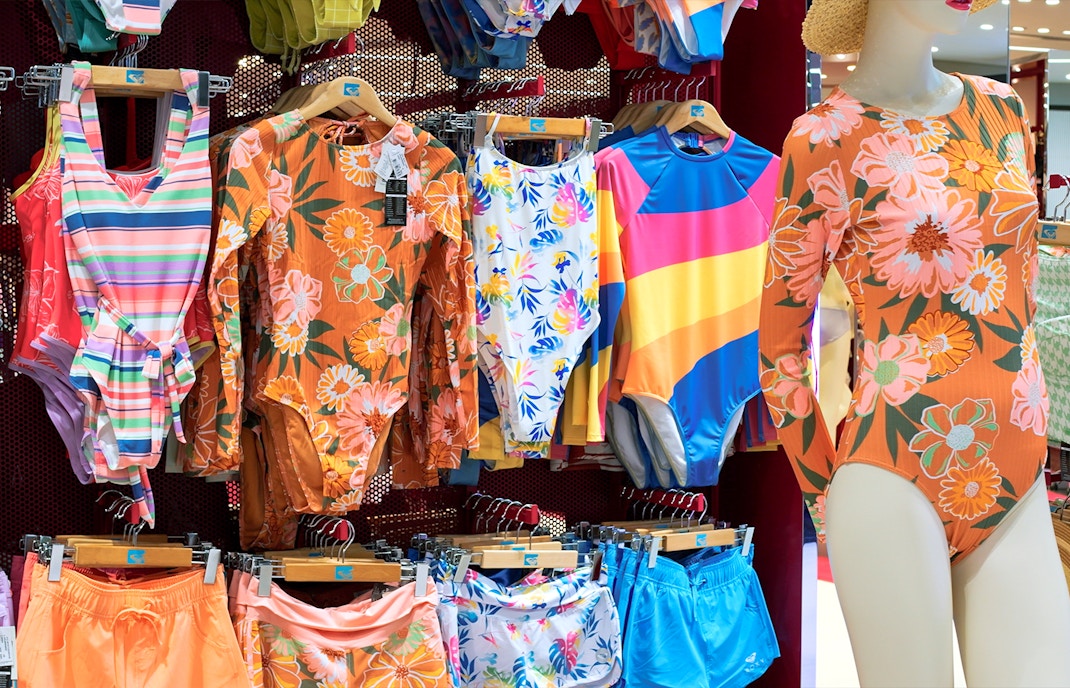 Swimwear display with colorful one-piece suits and shorts in a shop.