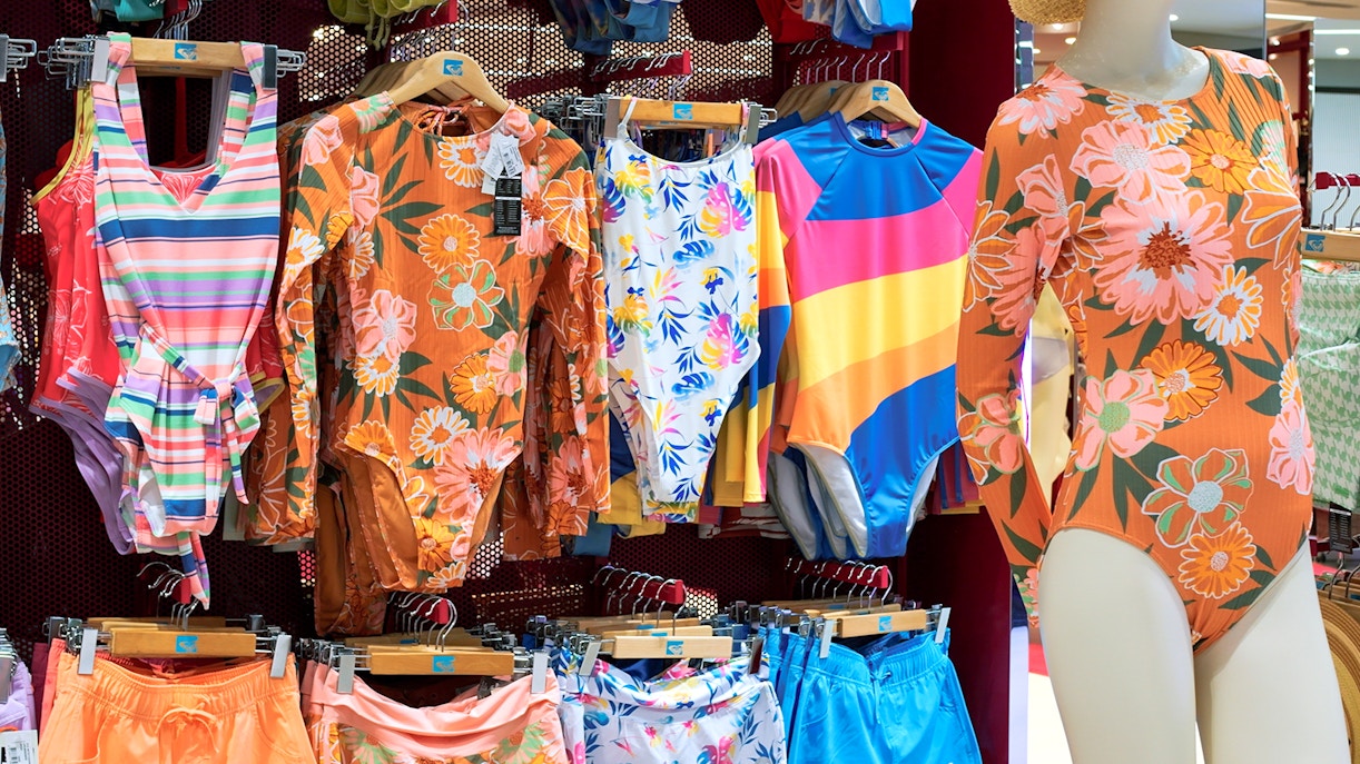 Swimwear display with colorful one-piece suits and shorts in a shop.