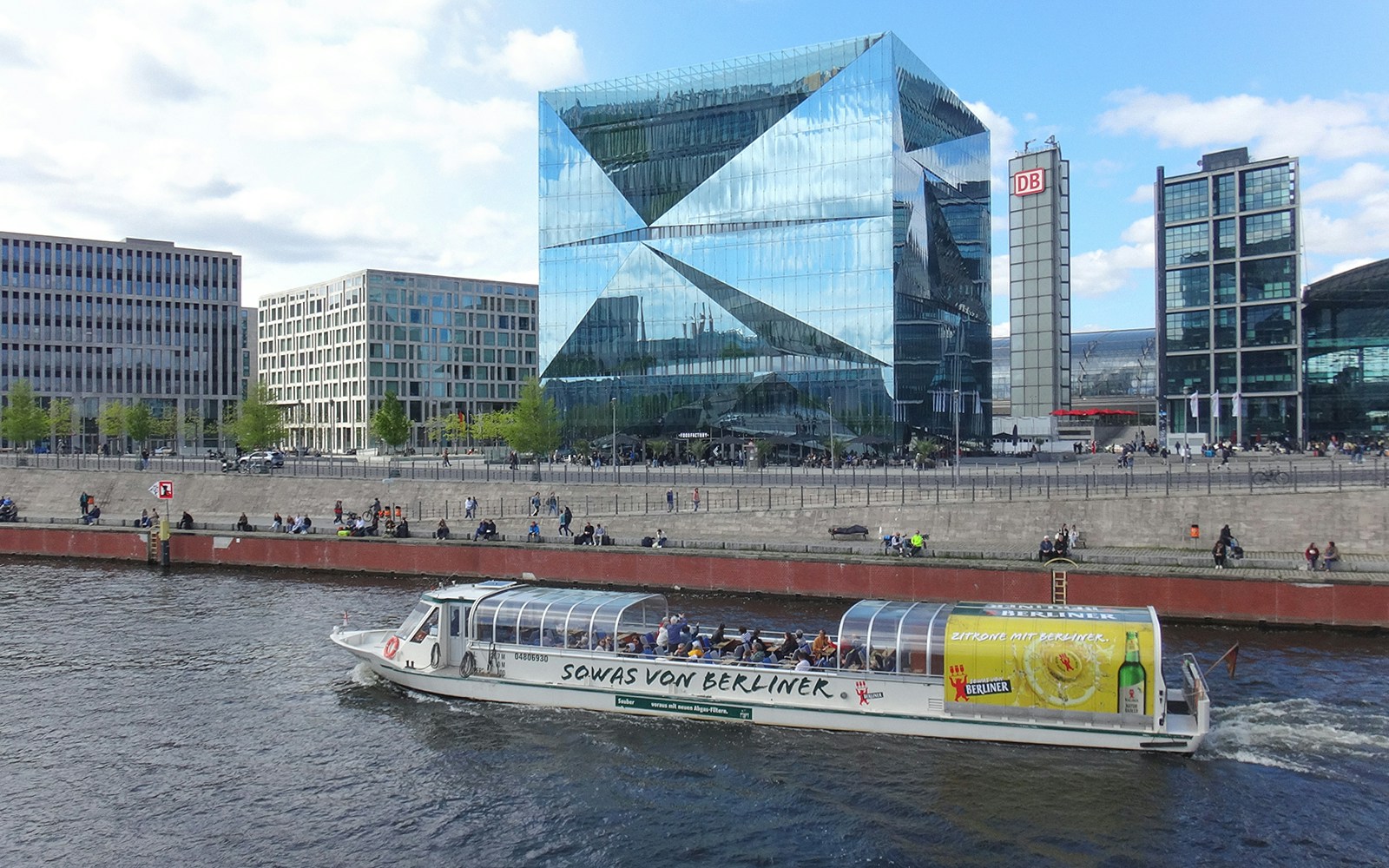 Berlin sightseeing cruise boat on the Spree River near modern glass buildings.