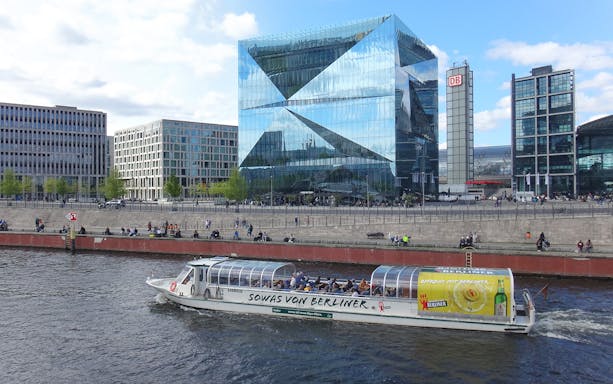 Berlin sightseeing cruise boat on the Spree River near modern glass buildings.