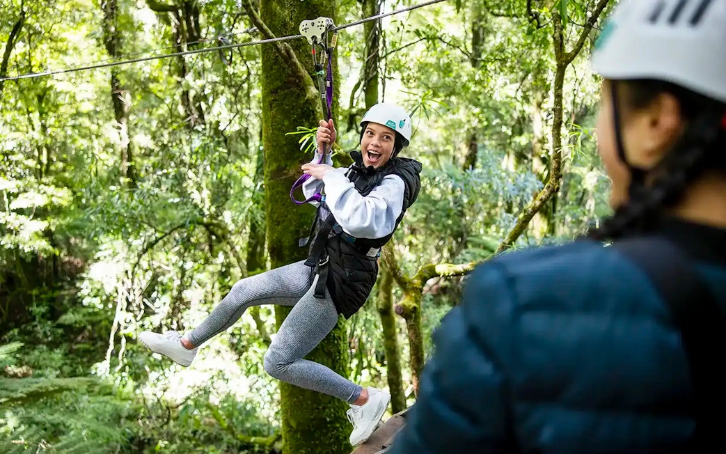 Person ziplining through lush Rotorua forest.